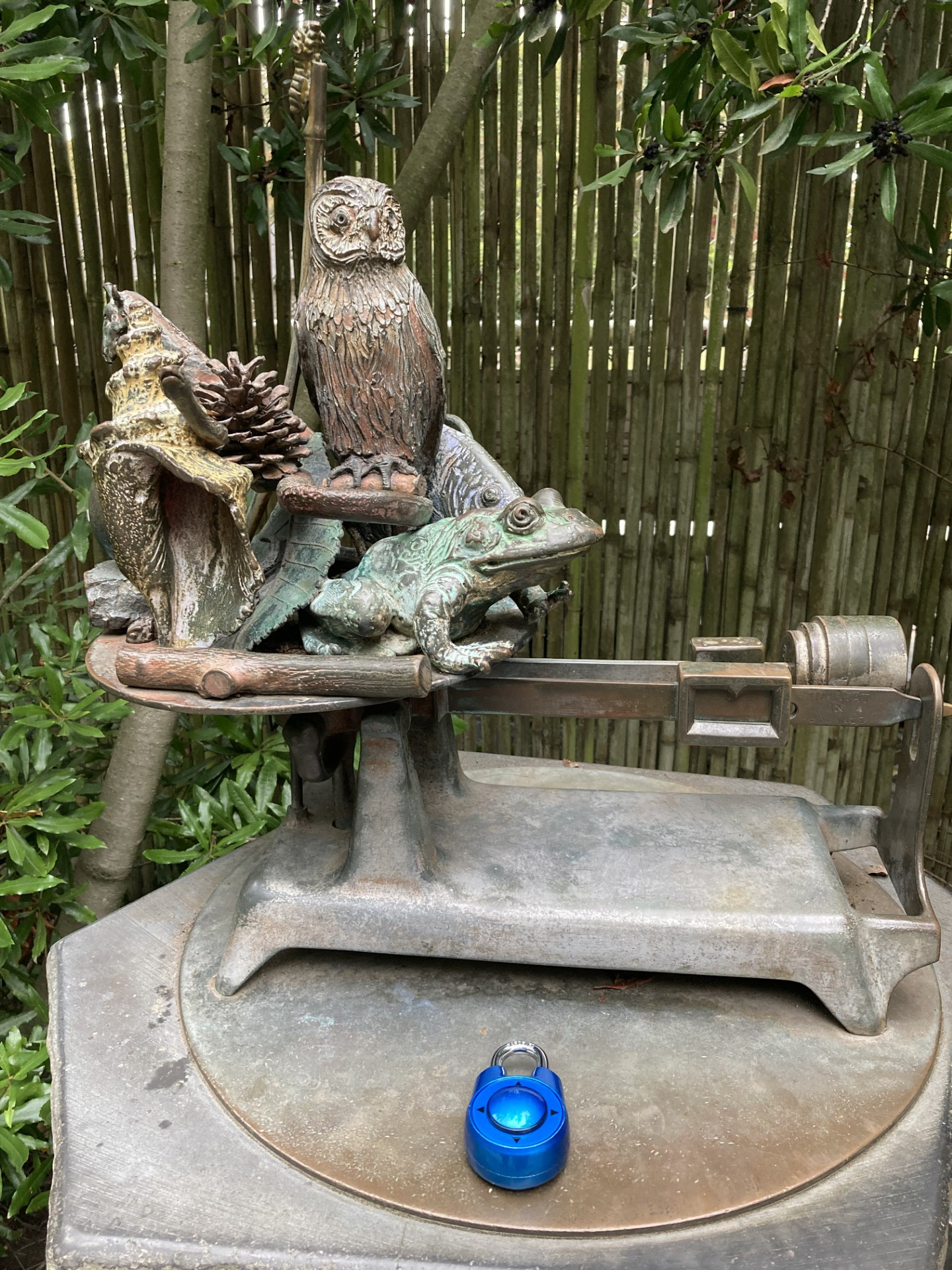 An image of a blue directional lock sitting on a bronze scale statue. The locking is facing up and pointing towards the scale